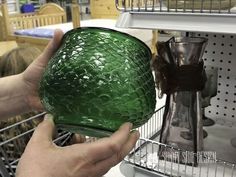 a person holding a green glass in front of a store shelf with other items on it