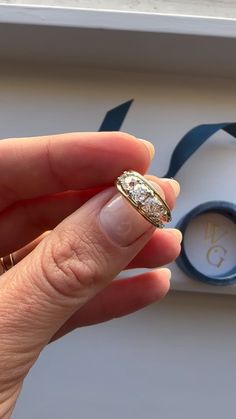 a woman's hand holding an engagement ring in front of a box with scissors