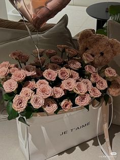 a teddy bear sitting on top of a white bag filled with pink roses and a heart shaped balloon