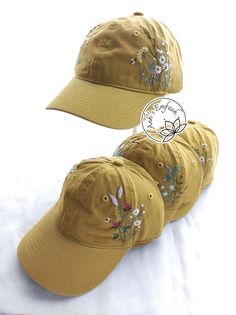 three hats with embroidered flowers on them sitting on top of a white bedding sheet