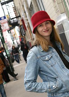 a woman wearing a jean jacket and red hat standing in front of a building on a city street