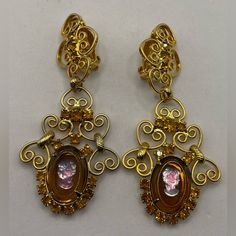 Gorgeous Vintage 1960s Celebrity By Juliana Ornate Cameo Statement Clip On Earrings Signed Celebrity On Back Of Clips. Dangling Gold Tone Earrings Feature Prong Set Amber Colored Oval Transparent Glass Cameos Inlaid With A Gold Tone Twisted Wire And A Blue And Pink Iridescent Woman's Profile In The Center. Accented With Citrine Colored Crystals And Filigree Heart Shaped Scrolls. Attributed Delizza & Elster Juliana. 3” X 1 3/8”. Beautiful Quality And In Excellent Vintage Condition. Vintage Vtg Coquette Balletcore Cottagecore Beaded Jewelry Hippy Retro Mod Modern Boho Bohemian 40s 50s 60s 70s Accessory 80s 90s Y2k Necklace Multistrand Gem Crystal Choker Bracelet Art Deco Avon Monet Avon Vintage Jewelry, Victorian Yellow Gold Clip-on Earrings, Vintage Gold Filigree Clip-on Earrings, 70s Accessories, Vintage Yellow Gold Plated Clip-on Earrings, Luxury Yellow Gold Vintage Clip-on Earrings, Mod Jewelry, Bracelet Art, Y2k Necklace