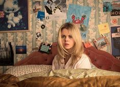 a woman sitting on top of a bed next to a wall covered in pictures and posters