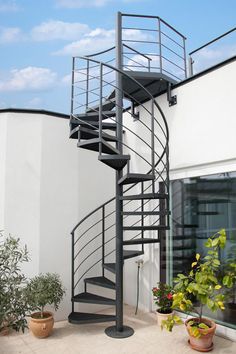 there is a metal spiral staircase on the side of a building with potted plants next to it