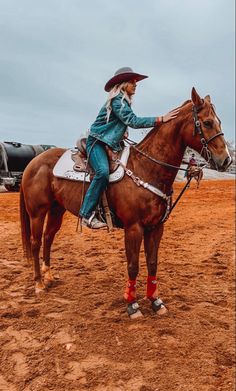 a woman riding on the back of a brown horse in a dirt field next to an airplane