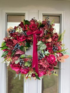 a wreath with red flowers and greenery hangs on the front door