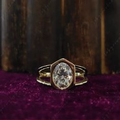 a gold ring with a white diamond in the center on a purple velvet covered surface