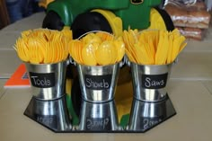 four silver cups filled with yellow flowers sitting on top of a counter next to a green toy tractor