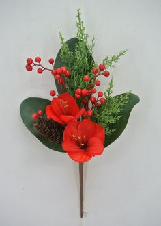 red flowers and greenery are arranged on a white wall with pine cones, berries, and evergreen