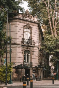 an old building on the corner of a street in front of trees and people sitting at tables