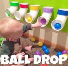 a baby is playing with balls in front of a wall mounted peg board that says ball drop