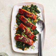 a white plate topped with meat and greens next to two silver spoons on top of a table