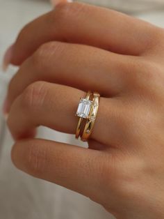 a woman's hand wearing two gold rings with an emerald stone in the middle