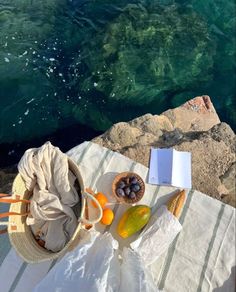 an open book and some fruit on a table by the ocean with water in the background