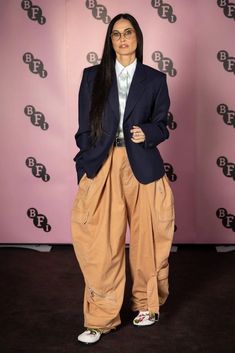 a woman standing in front of a pink wall wearing an oversized blazer and khaki pants