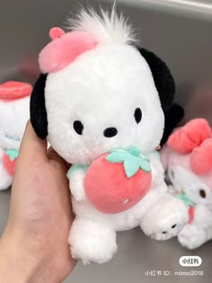 a hand holding a small white stuffed animal with pink and green bows on it's head