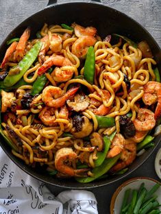 a skillet filled with shrimp, noodles and veggies on top of a table