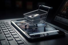 a shopping cart sitting on top of a cell phone next to a laptop computer keyboard