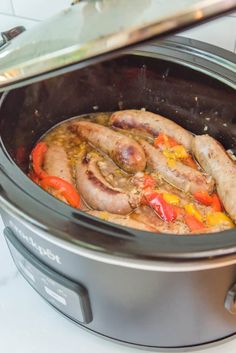 two sausages in a slow cooker with peppers and carrots on the side