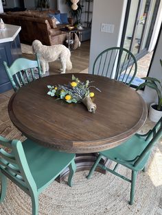 a dog standing next to a table with chairs and flowers on it in a living room