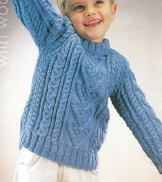 a young boy wearing a blue sweater and white pants with his arms in the air