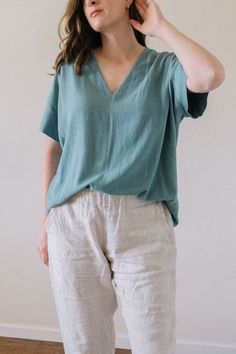 a woman standing in front of a white wall with her hand on her ear and wearing a green shirt