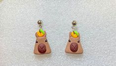 a pair of earrings with an animal head and fruit on the earring, sitting on a white surface