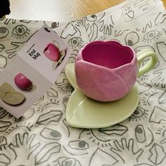 a pink cup and saucer sitting on top of a plate next to a box