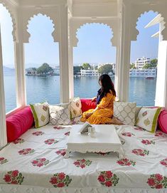 a woman sitting on top of a bed in front of a window next to the ocean