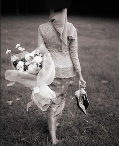 a woman walking in the grass holding a bouquet of flowers