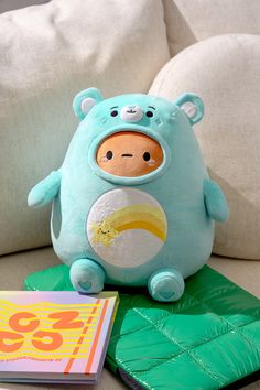 a blue stuffed animal sitting on top of a green blanket next to a book and pillow