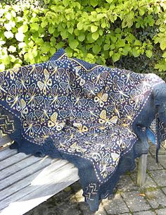 a blue and white blanket sitting on top of a wooden bench next to green bushes