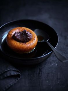 a chocolate covered donut on a black plate with a spoon and napkin next to it