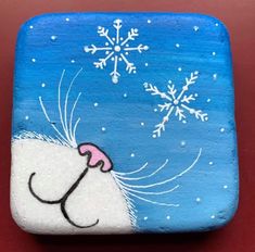 a painted square with snowflakes and a cat's nose on it, sitting on a red surface