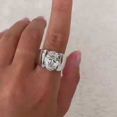 a person's hand holding a ring with a diamond in the middle and a white background