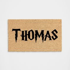 a door mat with the word thomas printed in black on it, against a white wall