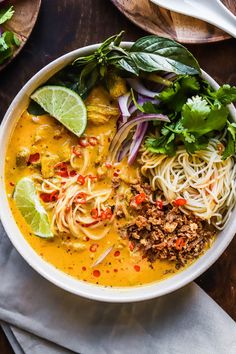 a white bowl filled with noodles, meat and veggies on top of a wooden table