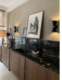 a kitchen with black marble counter tops and wooden cabinetry, along with pictures on the wall