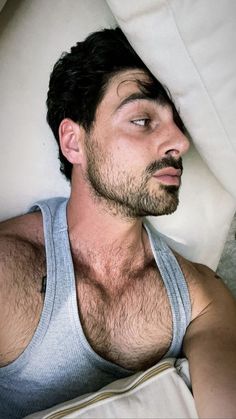 a shirtless man laying in bed with his eyes closed and looking at the camera