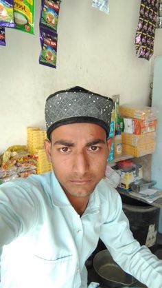 a man wearing a hat sitting at a table with food on the counter behind him