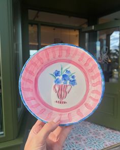 a hand holding a pink and blue plate with flowers on it