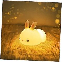 a white rabbit lamp sitting on top of a furry floor next to a light bulb