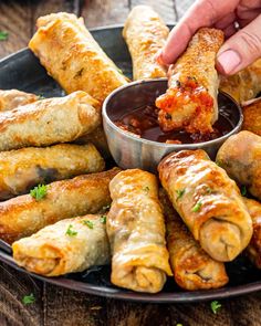 a person dipping sauce onto some food on a plate with other foods in the background