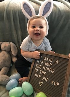 a baby sitting on a couch holding up a sign with bunny ears in front of it