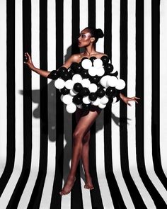 a woman standing in front of a black and white striped wall with balloons on it