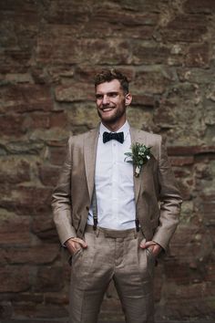 a man standing in front of a brick wall wearing a suit and bow tie