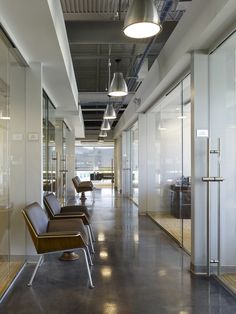 an empty office hallway with chairs and lamps hanging from the ceiling in front of glass walls