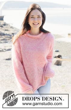 a woman standing on the beach wearing a pink sweater