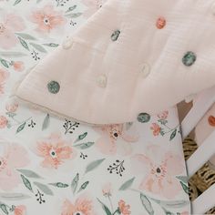 a baby crib with pink and green flowers on it's bedding, next to a wicker basket