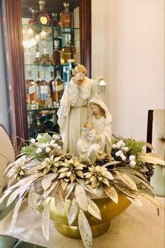 a statue of the virgin mary and jesus surrounded by greenery in front of a china cabinet